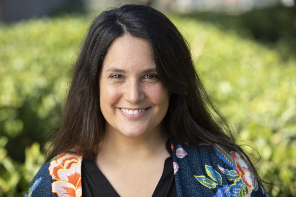 Foto de Isabel Contrucci sonriendo. De fondo se ven hojas verdes de un parque.