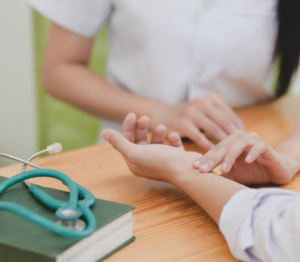 Foto de las manos de una doctora atendiendo a otra persona tocándole las manos. Sobre la mesa donde están apoyados sus brazos se ve un estetoscopio. 