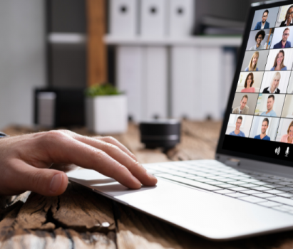 Foto de la mano de una persona tocando un computador portátil. En la pantalla del computador se ven varias personas conectadas por videollamada.