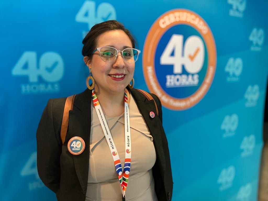 Foto de Javiera Gutiérrez sonriendo. Lleva una chapita que dice 40 horas y detrás hay un pendón que también dice "certificación 40 horas".