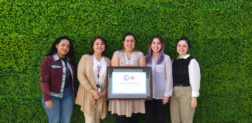 Foto de 5 mujeres de pie y sonriendo. La persona del medio sostiene un cuadro con una certificación del sello 40 horas.