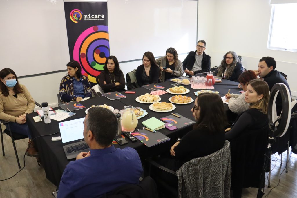 Investigadores asociados MICARE, miembros de la oficina de vocerías e invitados de Milenio reunidos alrededor de una mesa viendo presentaciones.