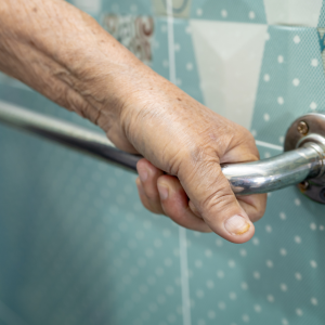 Foto de la mano de una persona mayor tomando un pasamanos en un baño.