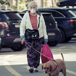 Foto de una mujer mayor con mascarilla caminando por la calle con una bolsa y paseando a un perro